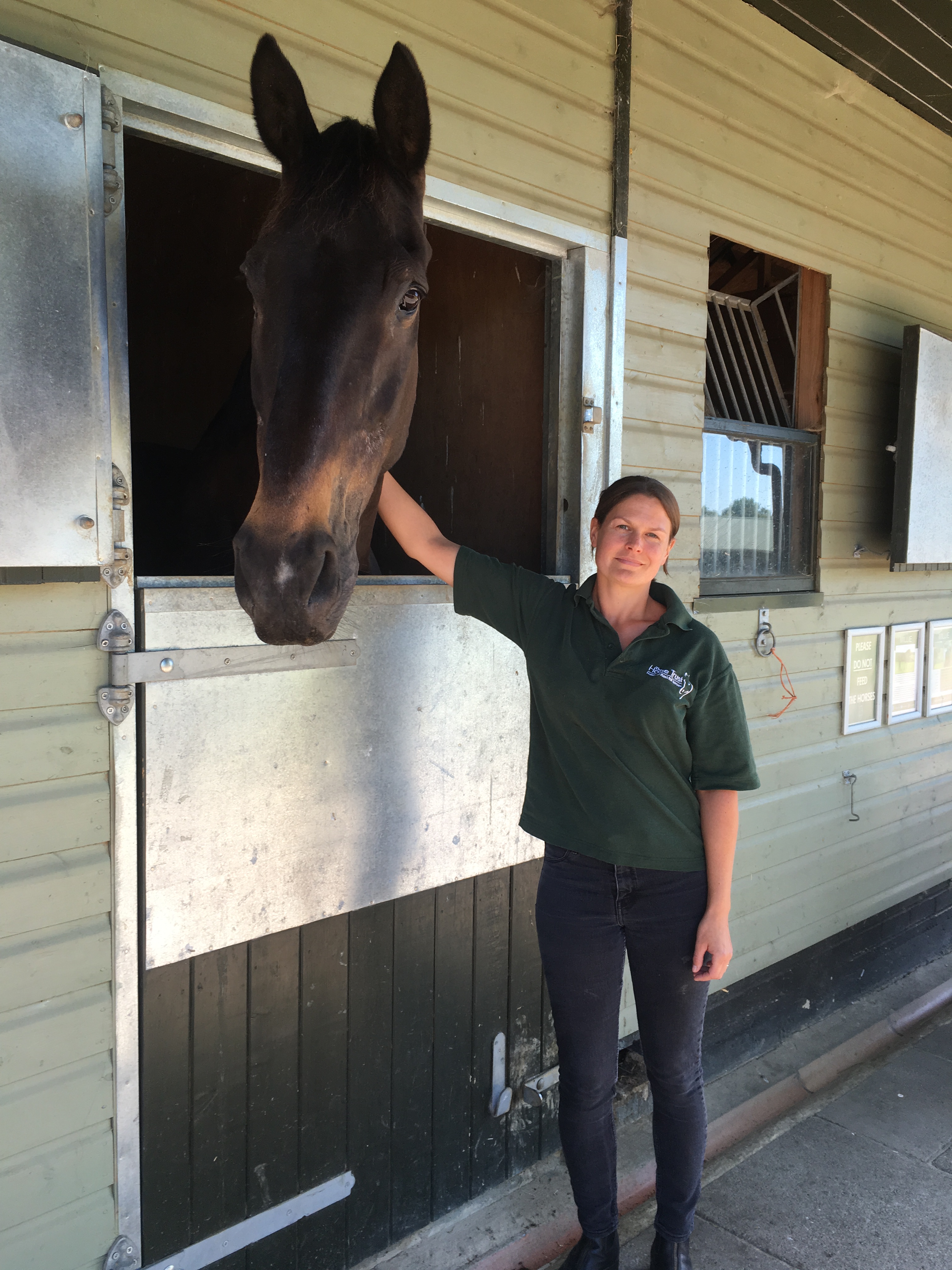 Liane standing outside stables, stroking a horse inside